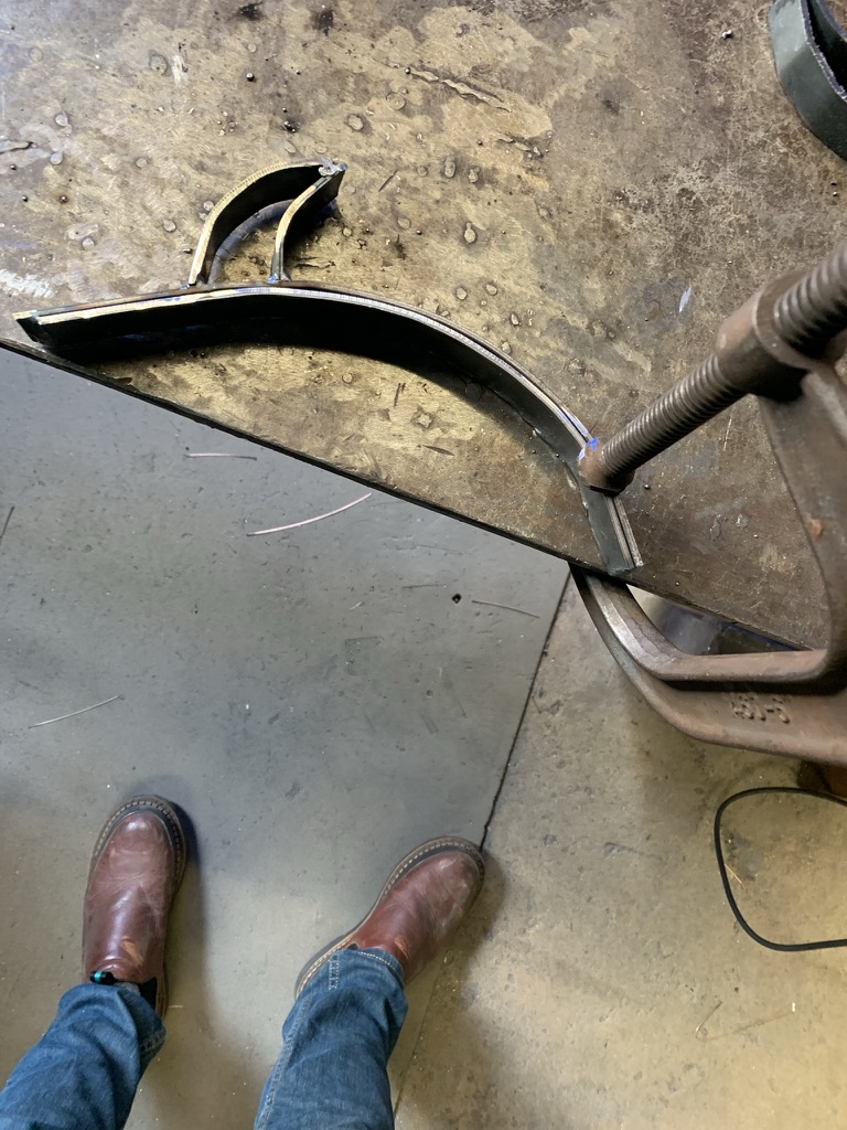 Curved steel stem clamped to a workbench during welding